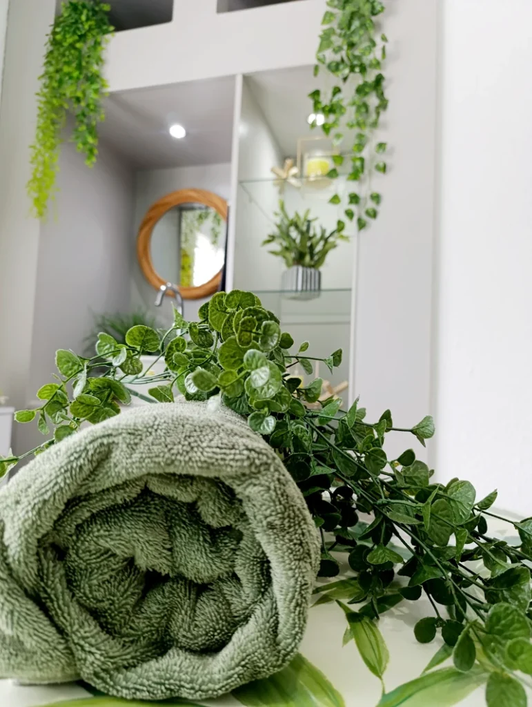 Rolled green towel with fresh green foliage in a tranquil spa setting.