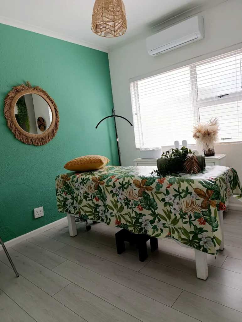 Bright treatment room with a floral-covered massage bed and natural decor.