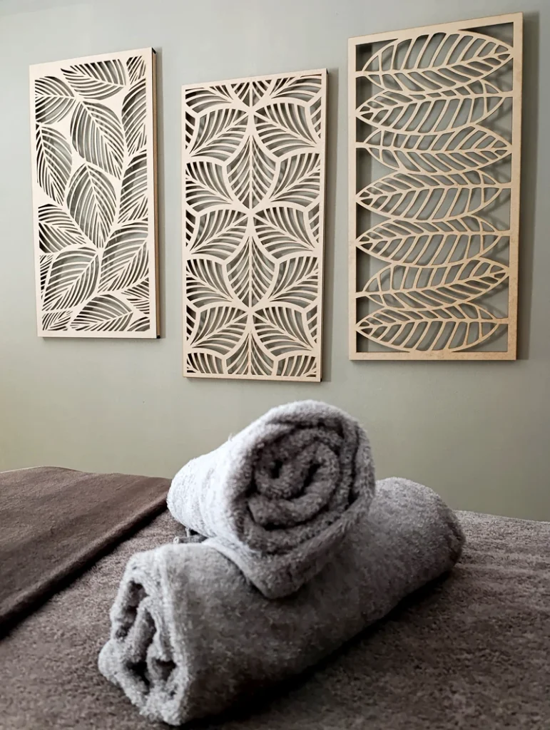 Neatly rolled grey towels on a treatment bed with decorative wooden wall art.
