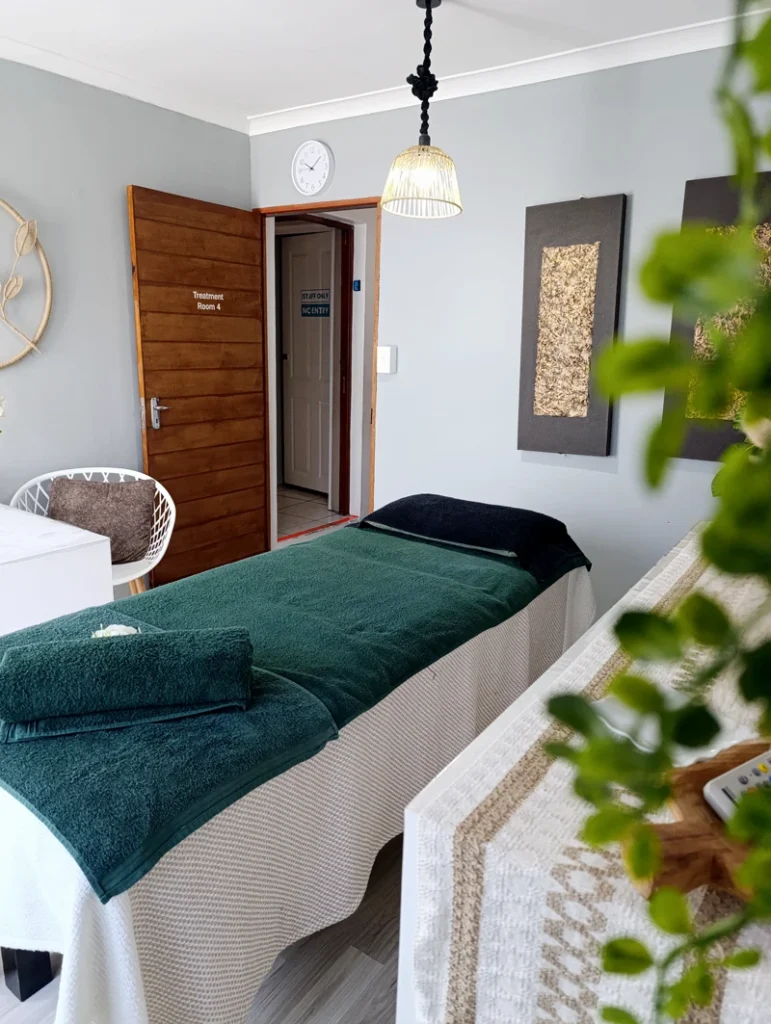 Spa room featuring botanical elements and a welcoming massage bed with green towels and fresh flowers.